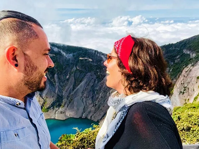 A man and a woman smiling at each other with a volcano crater in the background.