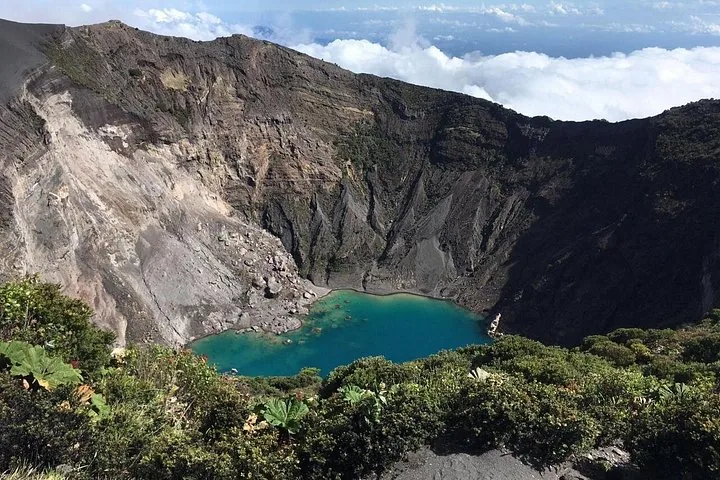 Vista hacia un profundo cráter volcánico que revela un lago turquesa brillante en el fondo