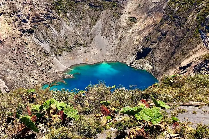 Una vista panorámica de un lago de cráter volcánico de color azul brillante rodeado de laderas rocosas.