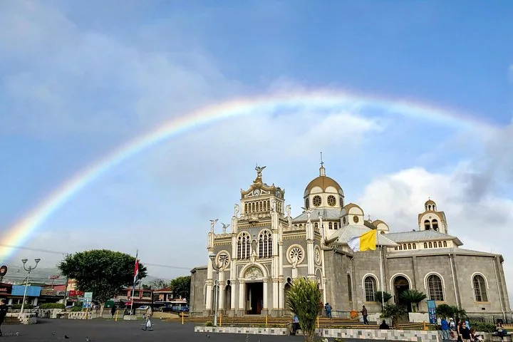 Ein großes, prunkvolles Kirchengebäude unter einem Himmel mit einem leuchtenden, vollständigen Regenbogen.