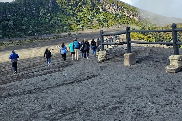 Group of tourists walking on a dark ash trail near a volcano