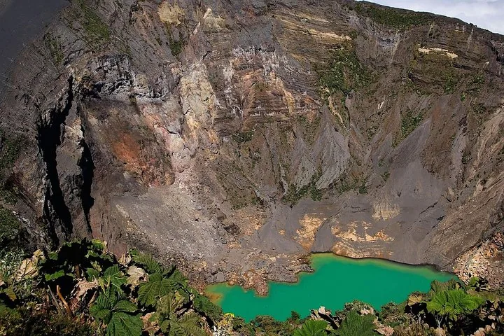 Ein tiefer Vulkankrater mit einem kleinen, leuchtend grünen See am Grund.