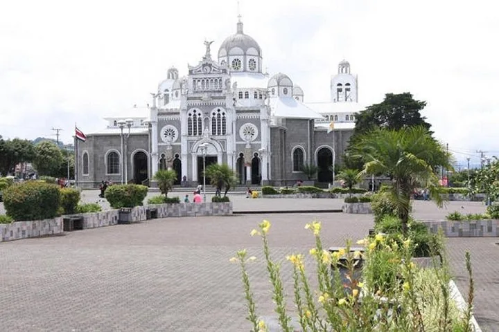 A grand stone church with white domes situated in a paved public plaza.